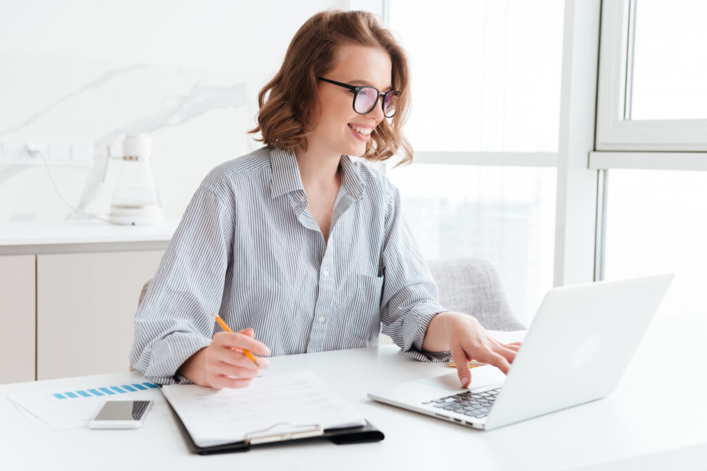 happy-brunette-businesswoman-glasses-using-laptop-computer-while-working-light-apartment
